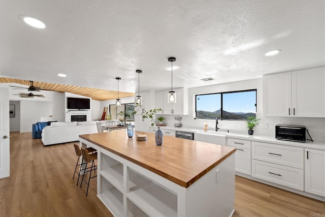 kitchen with a large fireplace, ceiling fan, light hardwood / wood-style flooring, white cabinets, and a kitchen island