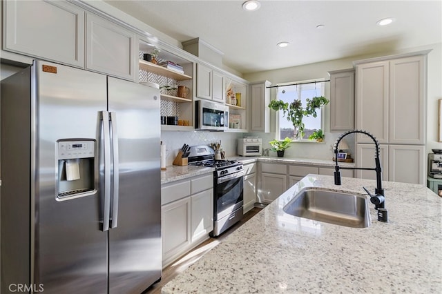 kitchen with gray cabinetry, light stone countertops, sink, appliances with stainless steel finishes, and hardwood / wood-style flooring