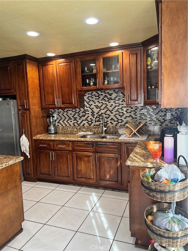 kitchen featuring decorative backsplash, stone countertops, stainless steel refrigerator, and sink