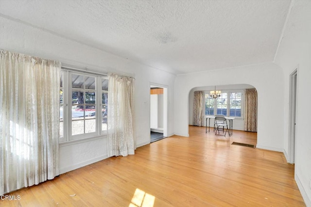 empty room with light wood-type flooring, a textured ceiling, and a chandelier