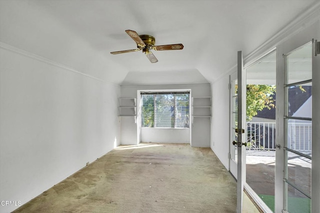 carpeted spare room with ceiling fan, vaulted ceiling, and ornamental molding