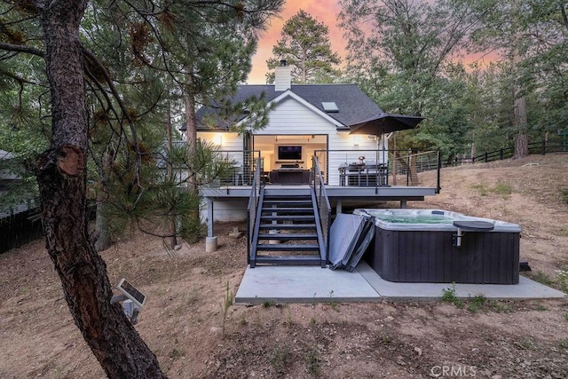 back house at dusk featuring a hot tub and a deck