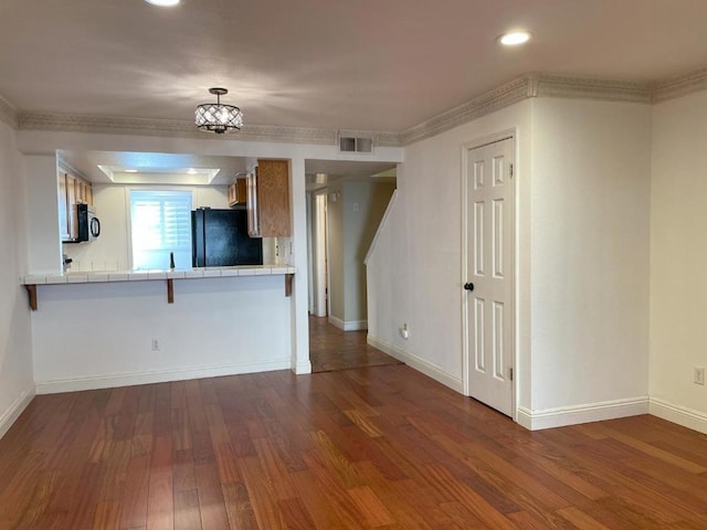 kitchen with dark wood-type flooring, black appliances, tile counters, and a breakfast bar area