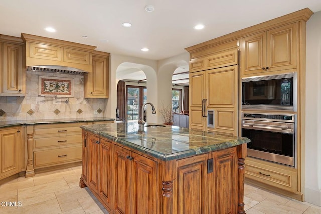 kitchen with oven, dark stone countertops, an island with sink, and black microwave