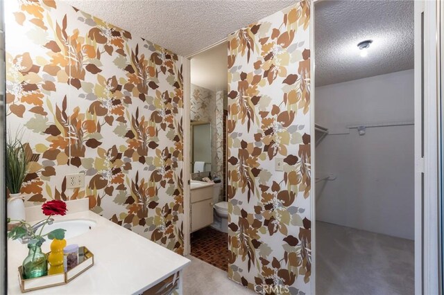 6542 Ocean Crest Dr Unit C-309, Rancho Palos Verdes, CA 90275 - bathroom featuring a textured ceiling, vanity, a spacious closet, and wallpapered walls