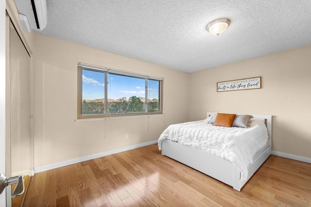 bedroom featuring a wall unit AC, a closet, light hardwood / wood-style flooring, and a textured ceiling