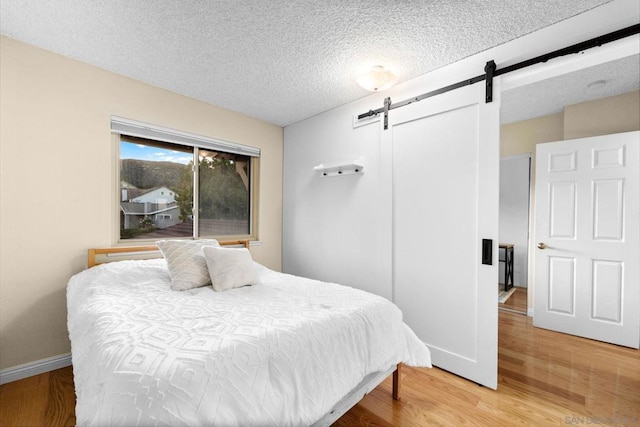 bedroom featuring a barn door, wood-type flooring, and a textured ceiling