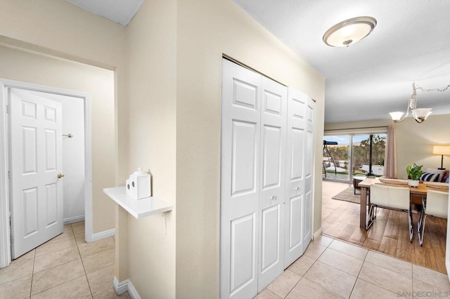 hallway with light tile patterned flooring and a notable chandelier