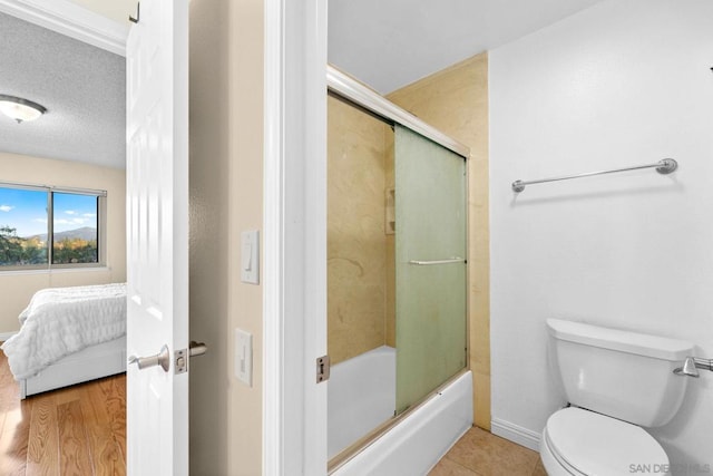 bathroom featuring hardwood / wood-style floors, bath / shower combo with glass door, a textured ceiling, and toilet