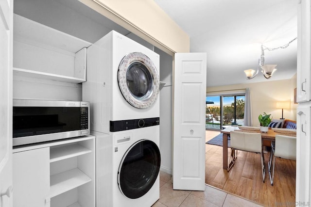 laundry room featuring light tile patterned floors, stacked washer / dryer, and an inviting chandelier