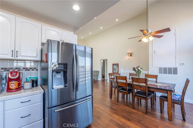 kitchen featuring dark wood-type flooring, stainless steel refrigerator with ice dispenser, ceiling fan, tile counters, and white cabinetry