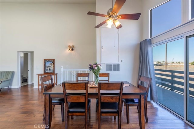 dining area with ceiling fan, dark hardwood / wood-style flooring, and a towering ceiling