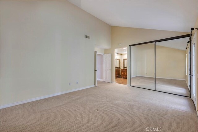 unfurnished bedroom featuring light carpet, a closet, ensuite bathroom, and high vaulted ceiling