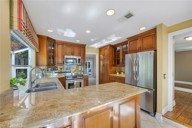 kitchen with kitchen peninsula, sink, stainless steel appliances, light tile patterned floors, and light stone counters