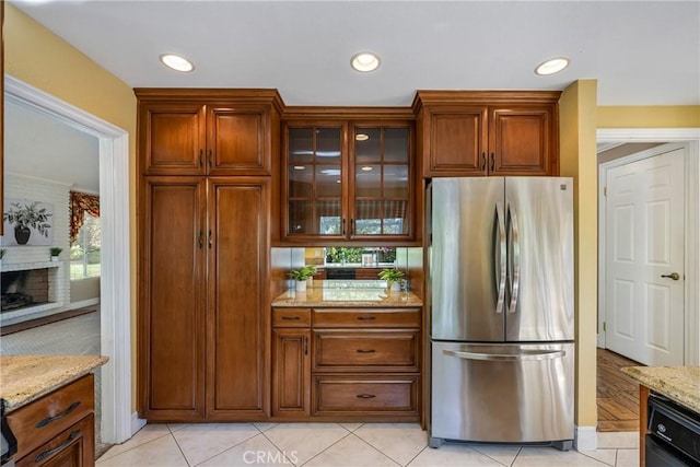 kitchen with light tile patterned floors, black dishwasher, light stone counters, and stainless steel refrigerator