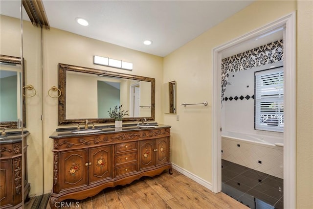 bathroom featuring vanity, wood-type flooring, and tiled tub