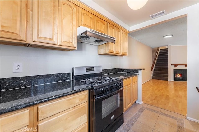 kitchen with dark stone countertops, black range with gas cooktop, light brown cabinetry, and light hardwood / wood-style flooring