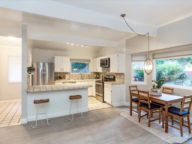 kitchen featuring white cabinetry, stainless steel appliances, tasteful backsplash, light hardwood / wood-style flooring, and a kitchen bar