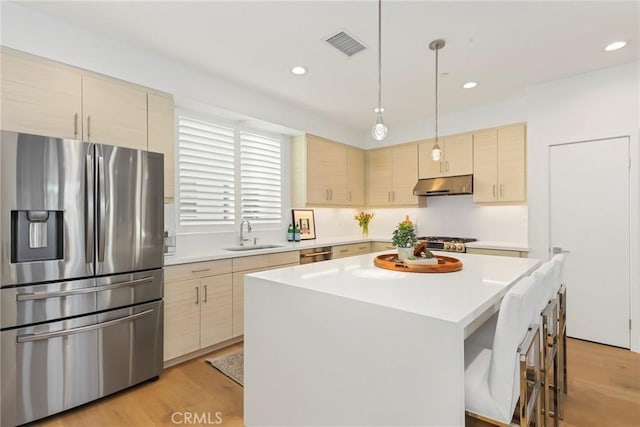 kitchen featuring appliances with stainless steel finishes, light brown cabinetry, sink, light hardwood / wood-style flooring, and a kitchen island