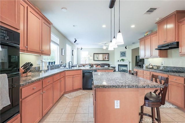 kitchen with a kitchen breakfast bar, hanging light fixtures, a center island, light tile patterned floors, and black appliances