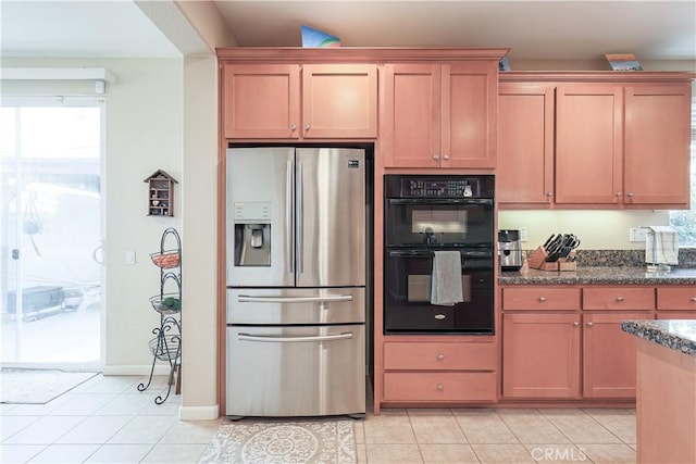 kitchen with stainless steel refrigerator with ice dispenser, black double oven, light tile patterned floors, and dark stone countertops