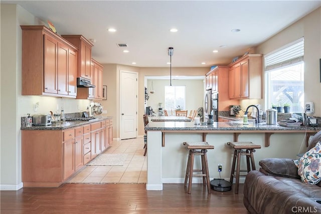 kitchen featuring a kitchen breakfast bar, hanging light fixtures, light hardwood / wood-style flooring, and dark stone countertops