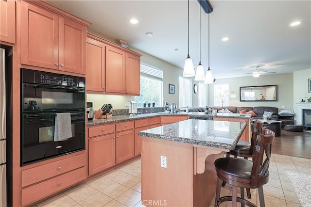 kitchen with pendant lighting, light tile patterned floors, dark stone countertops, double oven, and a center island