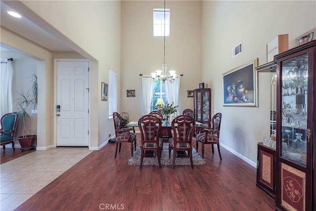 dining room featuring a towering ceiling, wood-type flooring, and a notable chandelier