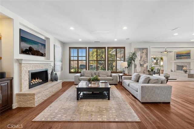 living room featuring ceiling fan, hardwood / wood-style flooring, and a stone fireplace