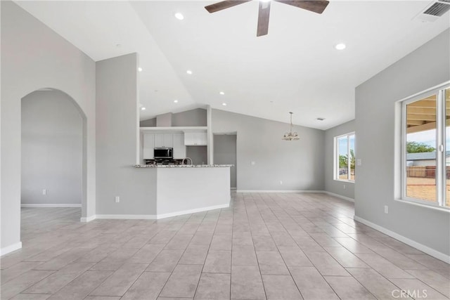 unfurnished living room featuring ceiling fan with notable chandelier and vaulted ceiling