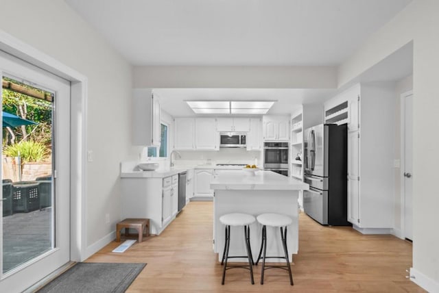 kitchen featuring a center island, light wood-type flooring, a kitchen bar, white cabinetry, and stainless steel appliances