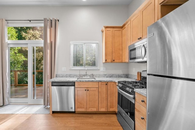 kitchen with light stone countertops, stainless steel appliances, light hardwood / wood-style floors, and sink