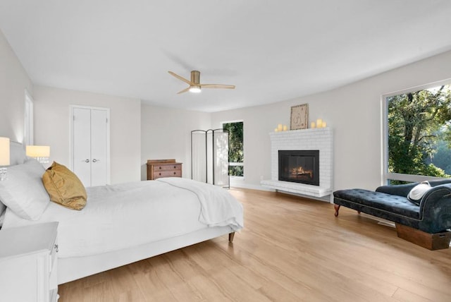 bedroom with a closet, ceiling fan, a fireplace, and light wood-type flooring