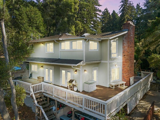 back house at dusk with a wooden deck and french doors