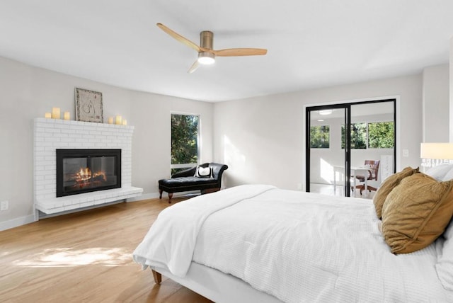 bedroom featuring hardwood / wood-style flooring, ceiling fan, access to outside, and a brick fireplace