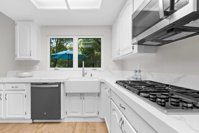 kitchen featuring light stone countertops, white cabinetry, sink, stainless steel appliances, and light wood-type flooring