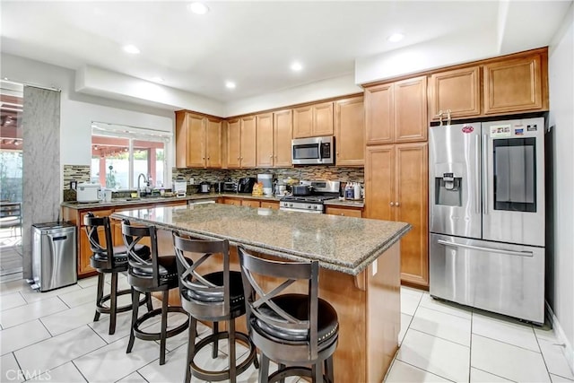 kitchen with a kitchen bar, appliances with stainless steel finishes, stone countertops, a kitchen island, and light tile patterned flooring