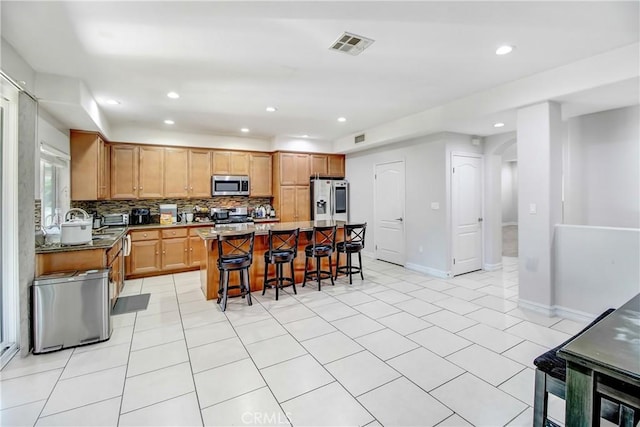 kitchen with a center island, tasteful backsplash, a breakfast bar area, light tile patterned floors, and appliances with stainless steel finishes