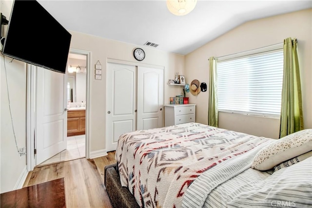 bedroom featuring connected bathroom, a closet, lofted ceiling, and light hardwood / wood-style flooring