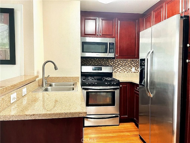 kitchen with sink, light stone counters, decorative backsplash, appliances with stainless steel finishes, and light wood-type flooring