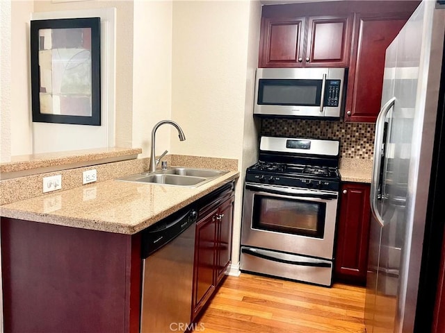 kitchen with backsplash, sink, light hardwood / wood-style flooring, light stone countertops, and stainless steel appliances