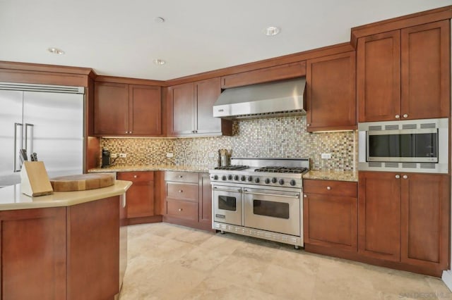 kitchen featuring built in appliances, wall chimney range hood, tasteful backsplash, and light stone countertops