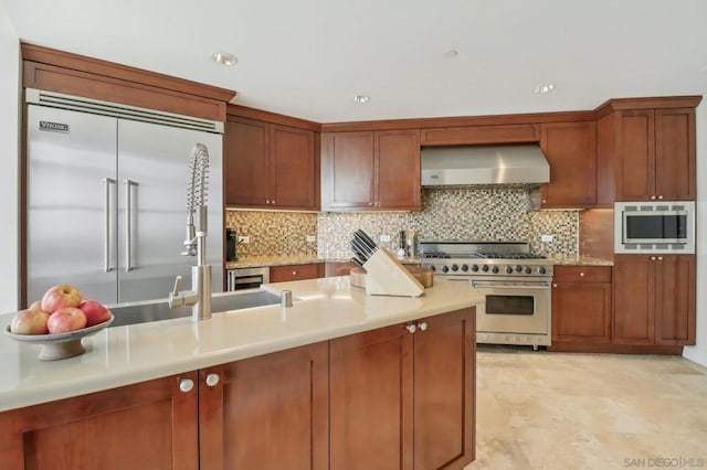 kitchen with built in appliances, decorative backsplash, and wall chimney range hood