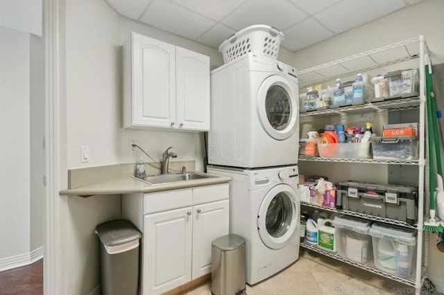 clothes washing area with sink, light tile patterned floors, cabinets, and stacked washer and clothes dryer