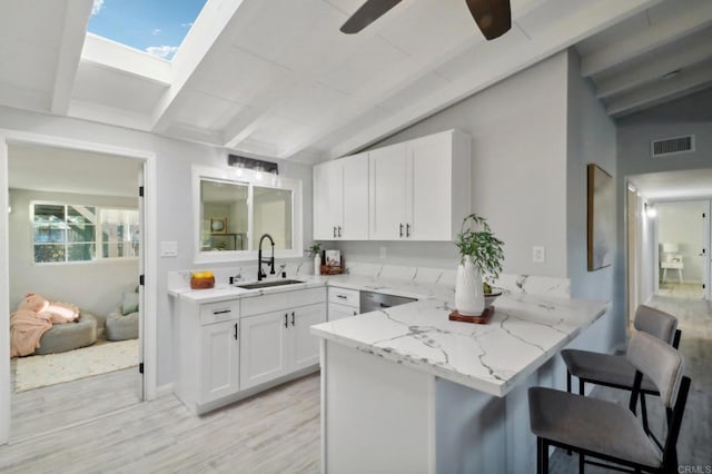 kitchen featuring a kitchen bar, lofted ceiling with skylight, sink, and white cabinets