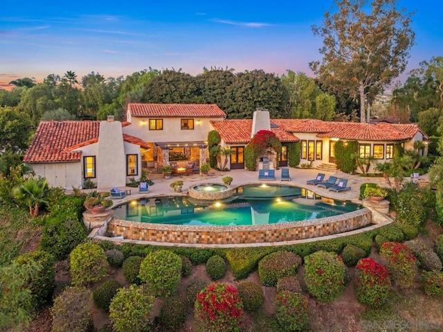 back house at dusk featuring a patio and a pool with hot tub