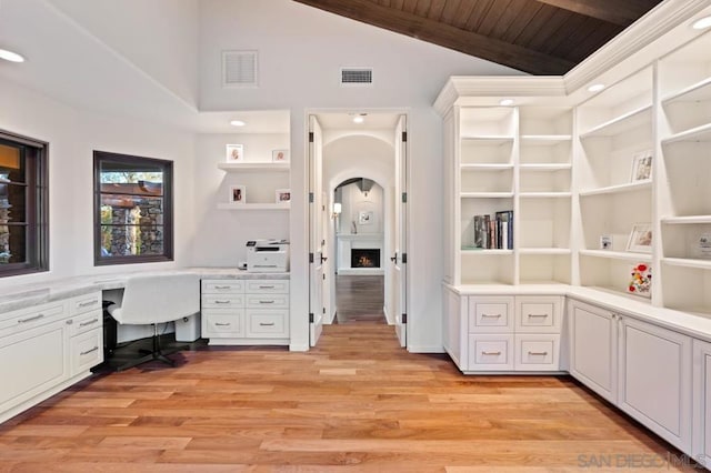 unfurnished office with vaulted ceiling with beams, wooden ceiling, built in desk, and light hardwood / wood-style floors