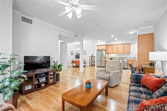 living room with ceiling fan with notable chandelier, ornamental molding, sink, and light hardwood / wood-style flooring