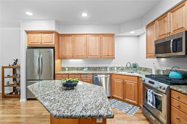 kitchen with light stone countertops, appliances with stainless steel finishes, light hardwood / wood-style flooring, and a kitchen island