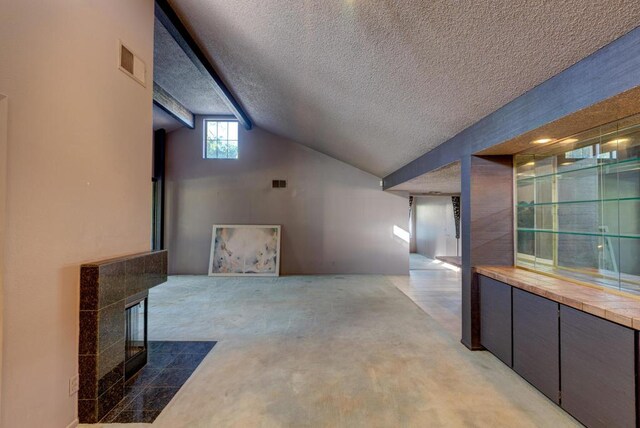 interior space with carpet floors, a textured ceiling, a tile fireplace, and lofted ceiling